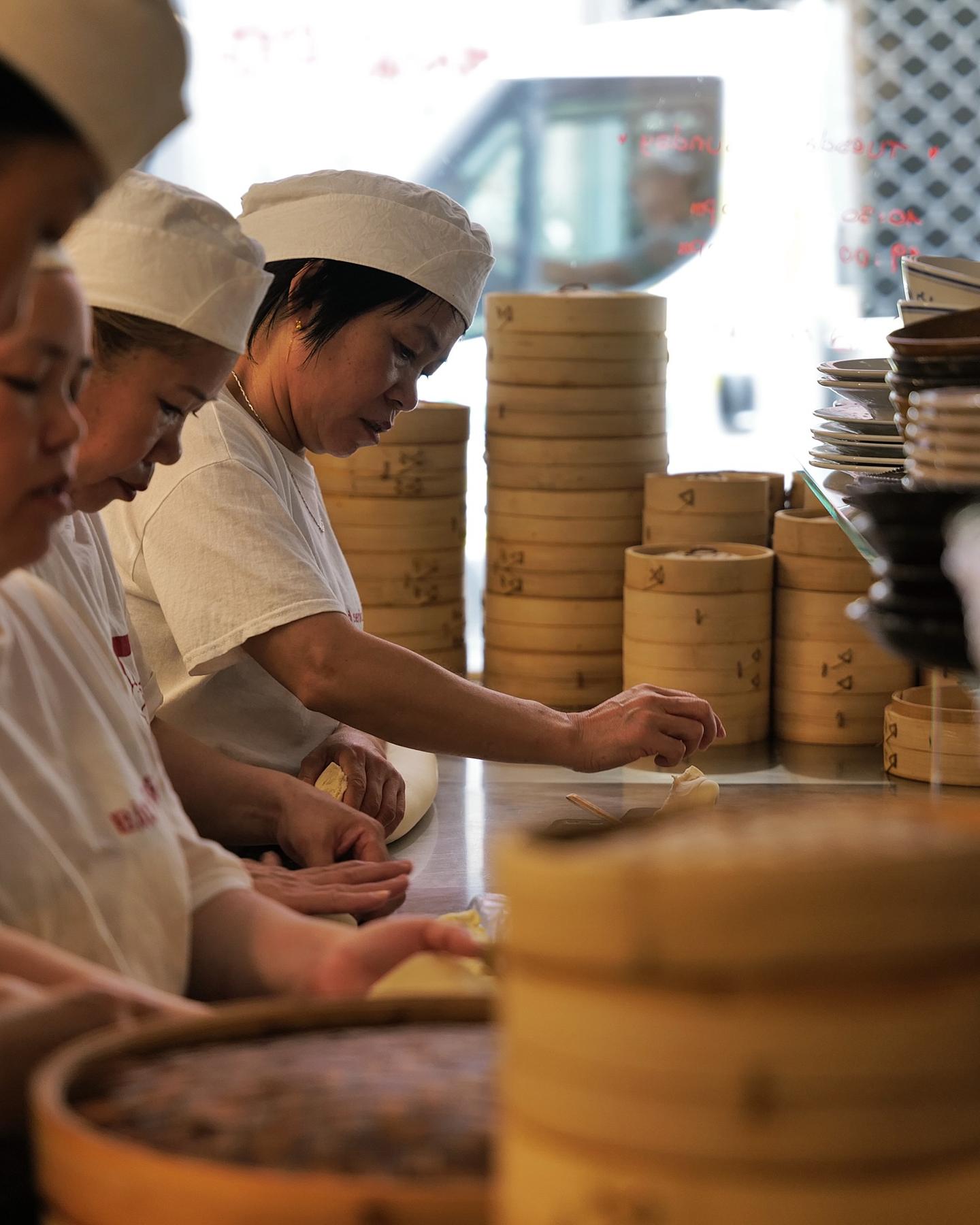 At the counter, four people in paper caps fold bao by hand, between stacks of bamboo steamers.