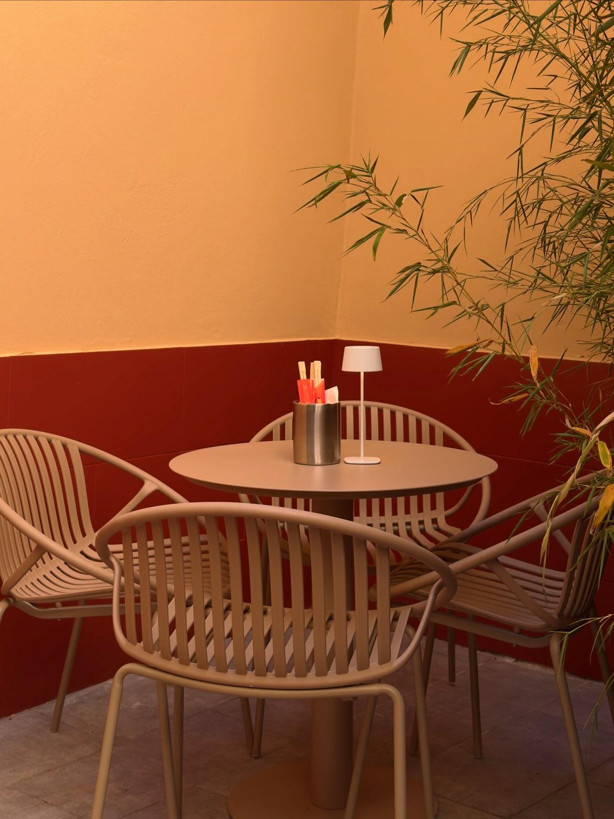 A corner of the garden, with pale chairs, a small table, a lamp and chopsticks.